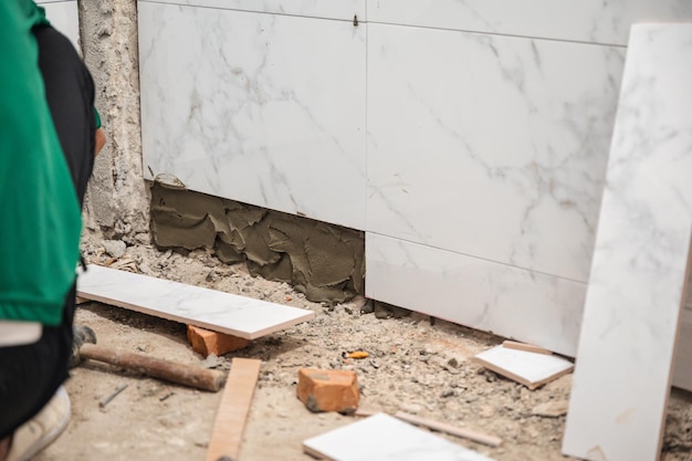 Mannelijke tegelzetter die een troffel gebruikt om marmeren tegels met cement in de badkamer te leggen Woningontwikkeling Renovatie van interieurverbetering