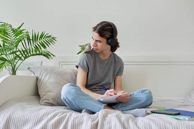 Mannelijke tiener met groene papegaai op zijn schouder met schoolboeken