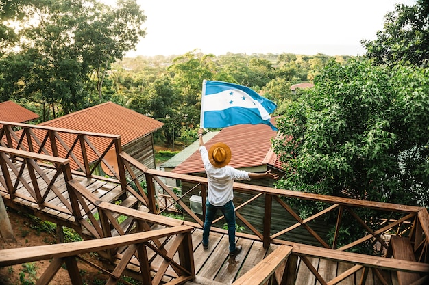 Mannelijke toerist die de vlag van Honduras zwaait voor enkele berghutten
