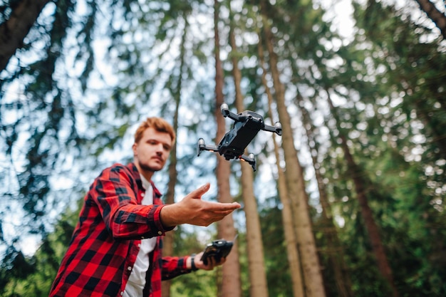 Mannelijke toerist met een afstandsbediening in zijn handen vliegt op een drone door een dicht zomerbos met een serieus gezicht De piloot lanceert de drone vanuit zijn handen en concentreert zich op de drone