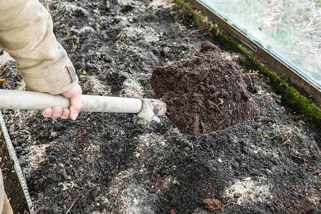 Mannelijke tuinman werknemer graven in moestuin met schop Boer man in rubberen laarzen werkende handen met spade graven zwarte grond grond gazon landbouwgrond landbouw herfst herfst lente werk schoonmaken