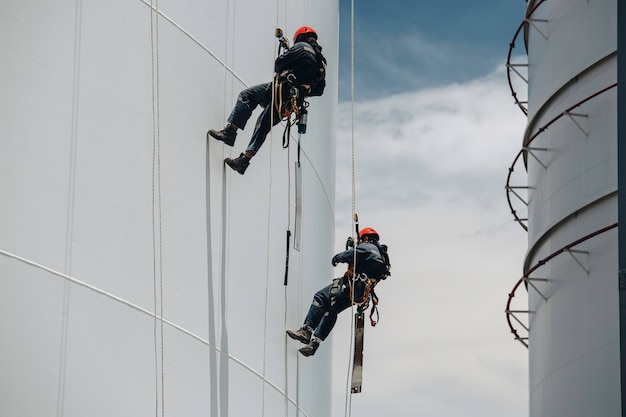 Mannelijke twee arbeiders controleren de hoogte van de schommelkabel naar beneden, de toegang tot de tankkabel, inspectie van de dikte van de pijpleiding en het tankgas