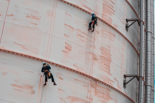 Mannelijke twee werknemer beneden hoogte tank dak touw toegang veiligheidsinspectie dikte las van opslagtank gas