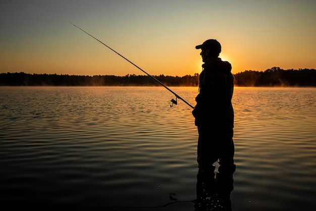 Mannelijke visser bij dageraad op het meer vangt een hengel Vissen hobby vakantie