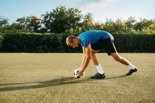 Mannelijke voetballer treft voorbereidingen om de bal op het veld te raken. Voetballer op buitenstadion, training voor de wedstrijd, voetbaltraining