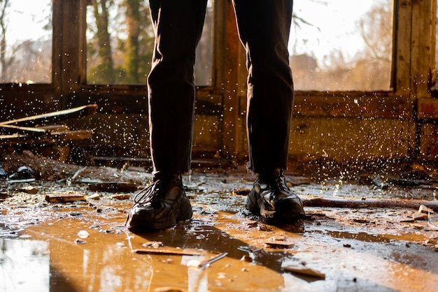 Mannelijke voeten tussen plassen en bevroren druppels in een overstroomd, verwoest en verlaten huis Zonnestralen