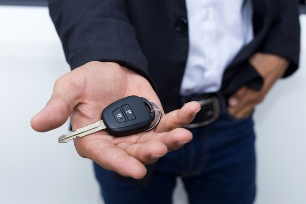 Mannelijke volwassen zakenman in een kostuum en een autosleutel in zijn hand houden. Witte auto's op de achtergrond