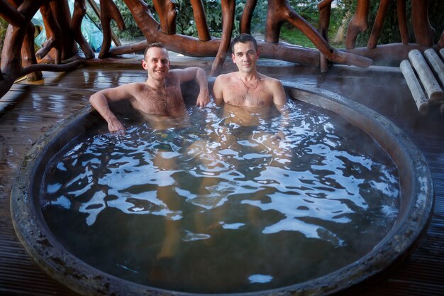 Mannelijke vrienden in het warmwaterzwembad op het terras, lichaamsbehandelingen in de spa. Buitenjacuzzi. Jacuzzi met vrienden. Ontspan in de open lucht. Huisje met bubbelbad.