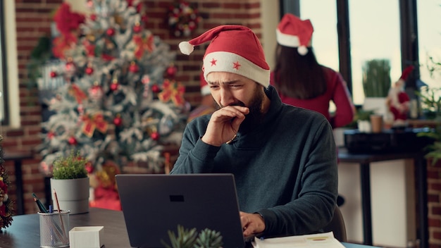 Mannelijke werknemer analyseert informatie over laptop op feestelijke werkplek, met behulp van computer tijdens kerstavond vakantie. Werken op pc in kantoor versierd met seizoensgebonden ornamenten. Uit de hand geschoten.