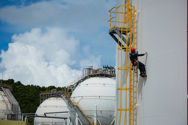 Mannelijke werknemer beneden touw toegang industrieel werken op hoogte tank olie dragen harnas, helm veiligheidsuitrusting touw toegang inspectie van dikte tank olie en gas achtergrond sferische propaan tanks.