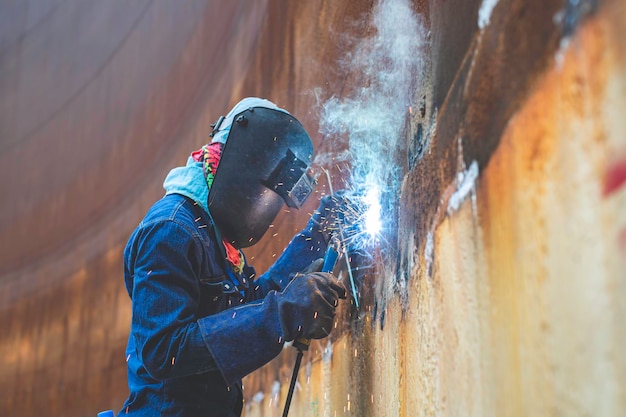 Mannelijke werknemer die beschermende kleding draagt en lasvonkschaal voor industriële constructie olie- en gas- of opslagtanks in besloten ruimtes repareert.