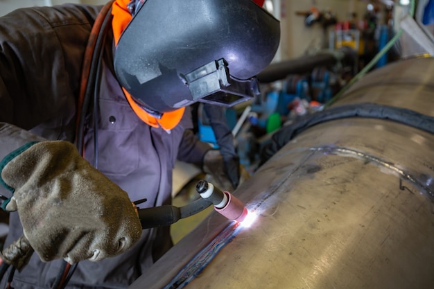 Mannelijke werknemer die beschermende kleding draagt van reparatiepijp roestvrij argon lassen industriële constructie