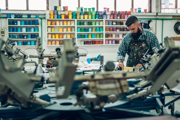 Mannelijke werknemer die inkt op het frame drukt tijdens het gebruik van de drukmachine in een werkplaats