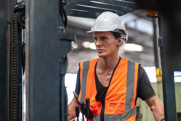 Mannelijke werknemer heftruckchauffeur in veiligheidsvest met helm werken in industriële fabriek logistiek verzendmagazijn