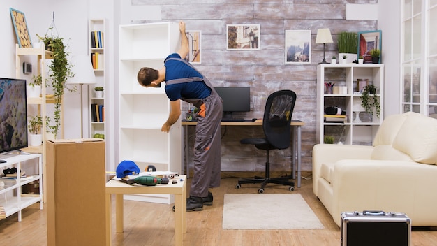 Mannelijke werknemer in overall haalt geassembleerde meubels op in het appartement van de eigenaar.