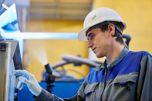 Mannelijke werknemer in overalls en helmpersen op de apparatuur van het touchscreen-bedieningspaneel in de fabriek