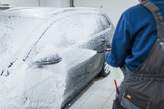 Mannelijke werknemer in uniform wassen van nieuwe moderne auto die bedekt is met zeep Conceptie van service