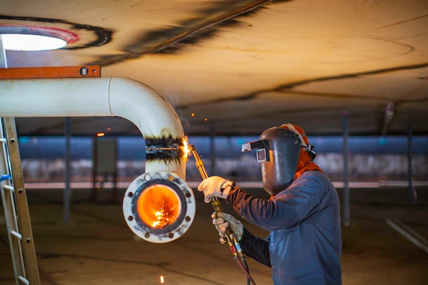 Mannelijke werknemer metalen pijpleiding elleboog snijden vonk op de tank met de flits van snijlicht close-up draag beschermende handschoenen en masker