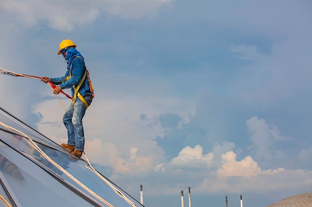 Mannelijke werknemers touwtoegangshoogte veiligheid verbinden met een knoopveiligheidsharnas, dakvalstop en valbeveiligingsankerpuntsystemen klaar om te stijgen, bouwplaatsolietankkoepel