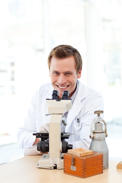Mannelijke wetenschapper die door een microscoop met exemplaar-ruimte kijkt