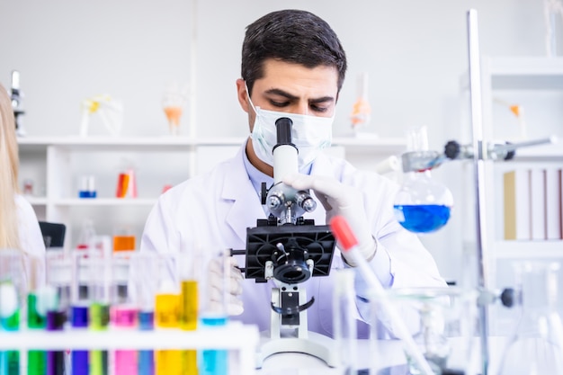 Mannelijke wetenschapper die Microscoop met steekproefreageerbuis bekijkt in een chemielaboratorium
