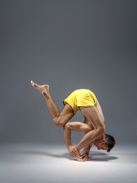 Mannelijke yoga in een moeilijke pose op handen, meditatie, grijze achtergrond.