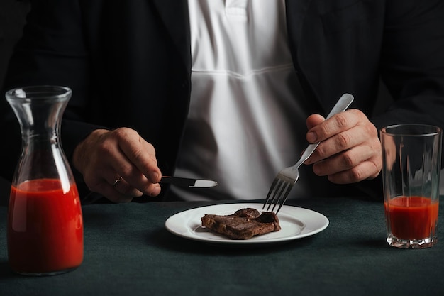 Mannelijke zakenman aan het eten van smakelijke gegrilde biefstuk en rood tomatensap