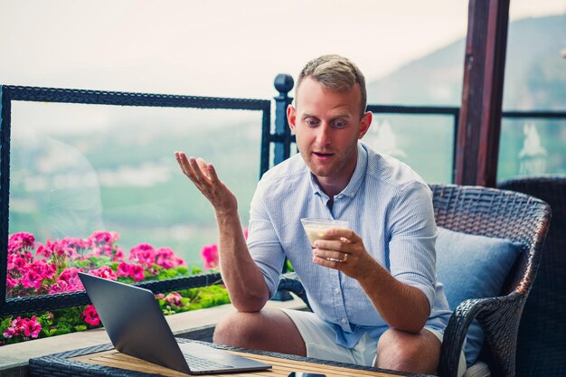 Mannelijke zakenman die op laptop werkt in café op het dak met prachtig panoramisch uitzicht Guy blogger drinkt koffie en werkt op een computer tijdens het reizen