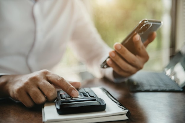 Mannelijke zakenmanhand die rekenmachine en smartphone gebruiken met berekenen over kosten op kantoor