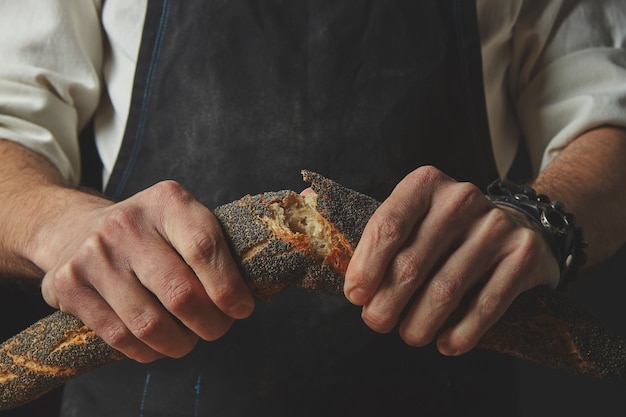 Mannen Hand breken en scheiden van een vers gebakken stokbrood met maanzaad. Concept van brood.