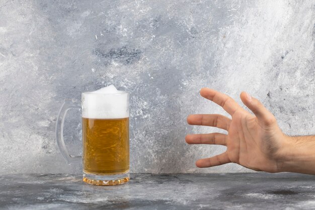 Mannen hand trekken aan glazen mok bier met schuim op stenen oppervlak