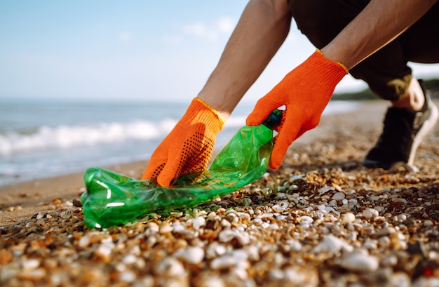 Mannen hand verzamelt plastic fles op zee strand.