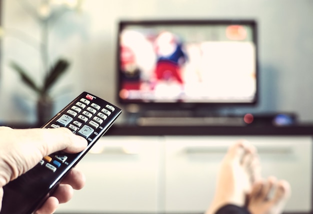 Mannen met de afstandsbediening voor de televisie. Hand met afstandsbediening gericht op de TV. Een man ontspant en kijkt naar sport op tv.