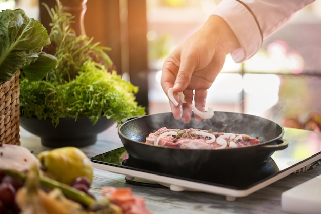 Mannen overhandigen koekenpan. Stukjes ui op vlees. Chef-kok maakt biefstuk met kruiden. Rundvlees voor het diner.