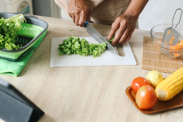 Mannen snijden sla in stukken met een mes op de snijplank terwijl ze thuis een salade bereiden