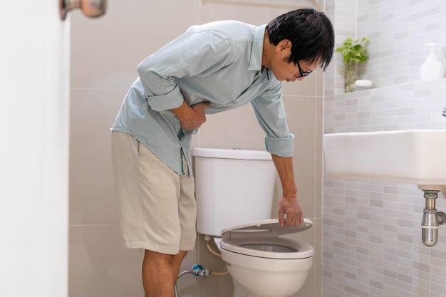 Mannen staan voor de deur van de badkamer met hun handen om de buik vast te houden met hevige buikpijn of diarree Het concept van maagkrampen diarree