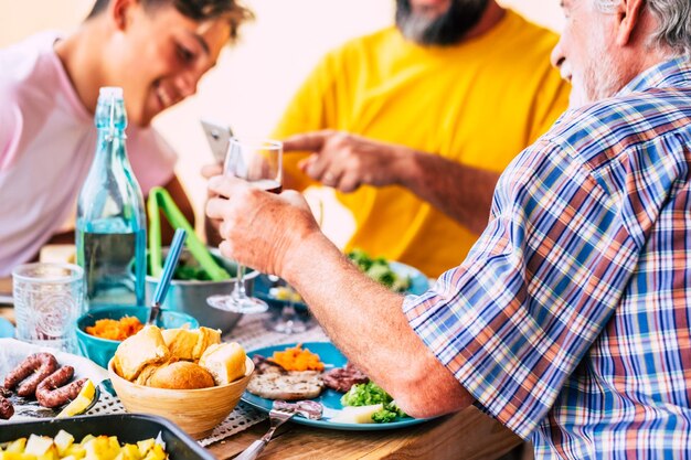 Foto mannen van drie generaties van dezelfde familie genieten van eten en drinken die naar de smartphone kijken blanke mensen houten tafel op het terrasveld