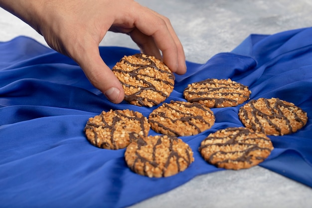 Mannenhand die havermoutkoekje nemen dat op blauw tafellaken wordt geplaatst.