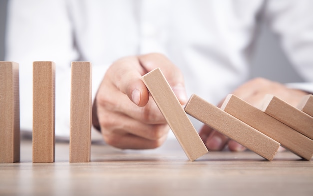 Mannenhand die houten domino tegenhoudt. Bedrijf. Crisis. Risico