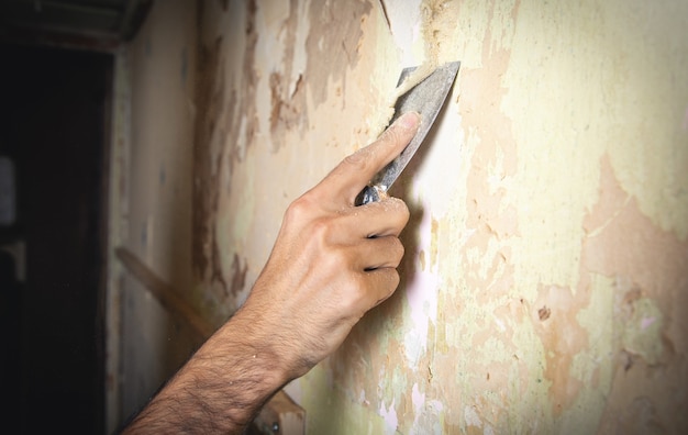 Mannenhand die oud behang van de muur verwijdert.