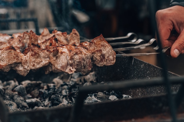 Mannenhand draait rauw gebakken vlees op spiesjes wordt gekookt op houtskoolgrill. buiten barbecueën