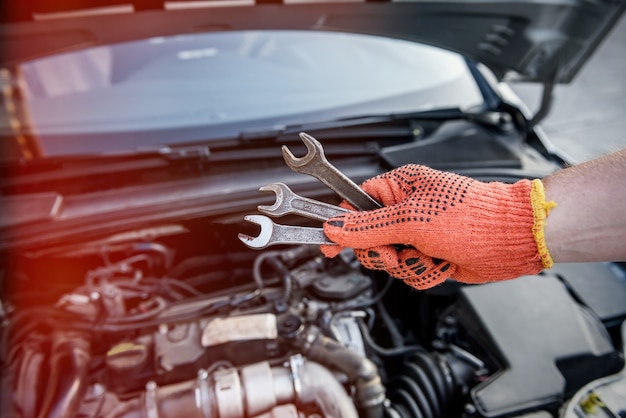 Mannenhand in handschoen met sleutels tegen automotor