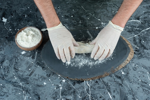 Mannenhand in handschoenen deeg maken op marmeren tafel.