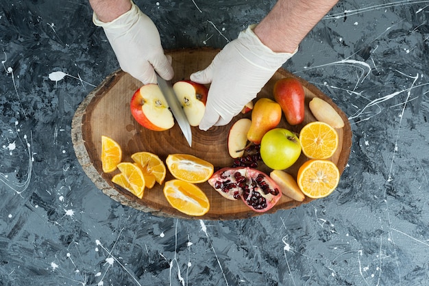 Mannenhand in handschoenen die verse appel op marmeren lijst snijden.