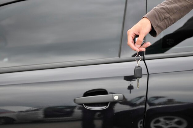 mannenhand met autosleutel met nieuwe zwarte auto op de achtergrond