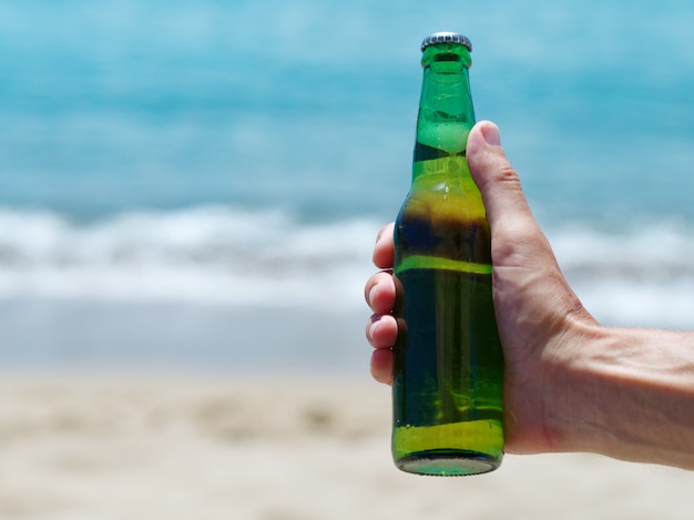 Mannenhand met flesje bier tegen oceaan zandstrand. Kopieer ruimte.