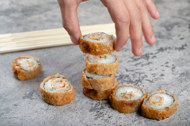 Mannenhand met hete gebakken sushi roll in de buurt van houten wegwerp eetstokjes.