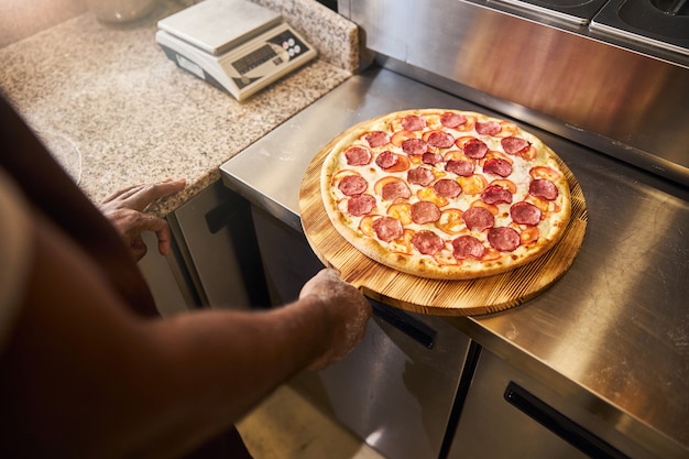 mannenhand met houten plank met versgebakken pizza met salami