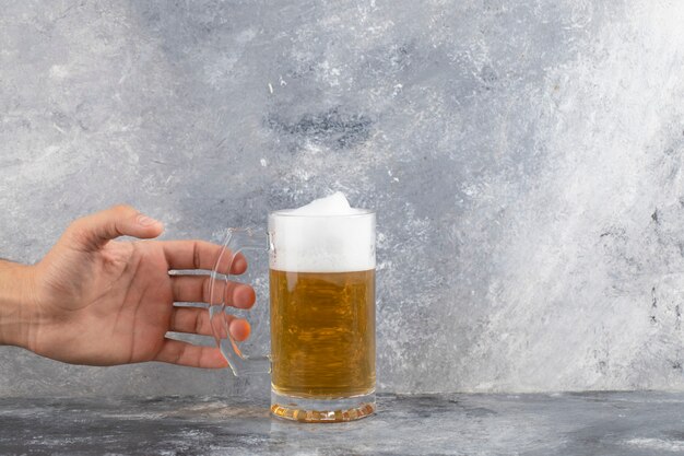 Mannenhand met mok koud schuimend bier op marmeren oppervlak