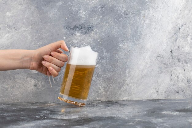 Mannenhand met mok koud schuimend bier op marmeren oppervlak